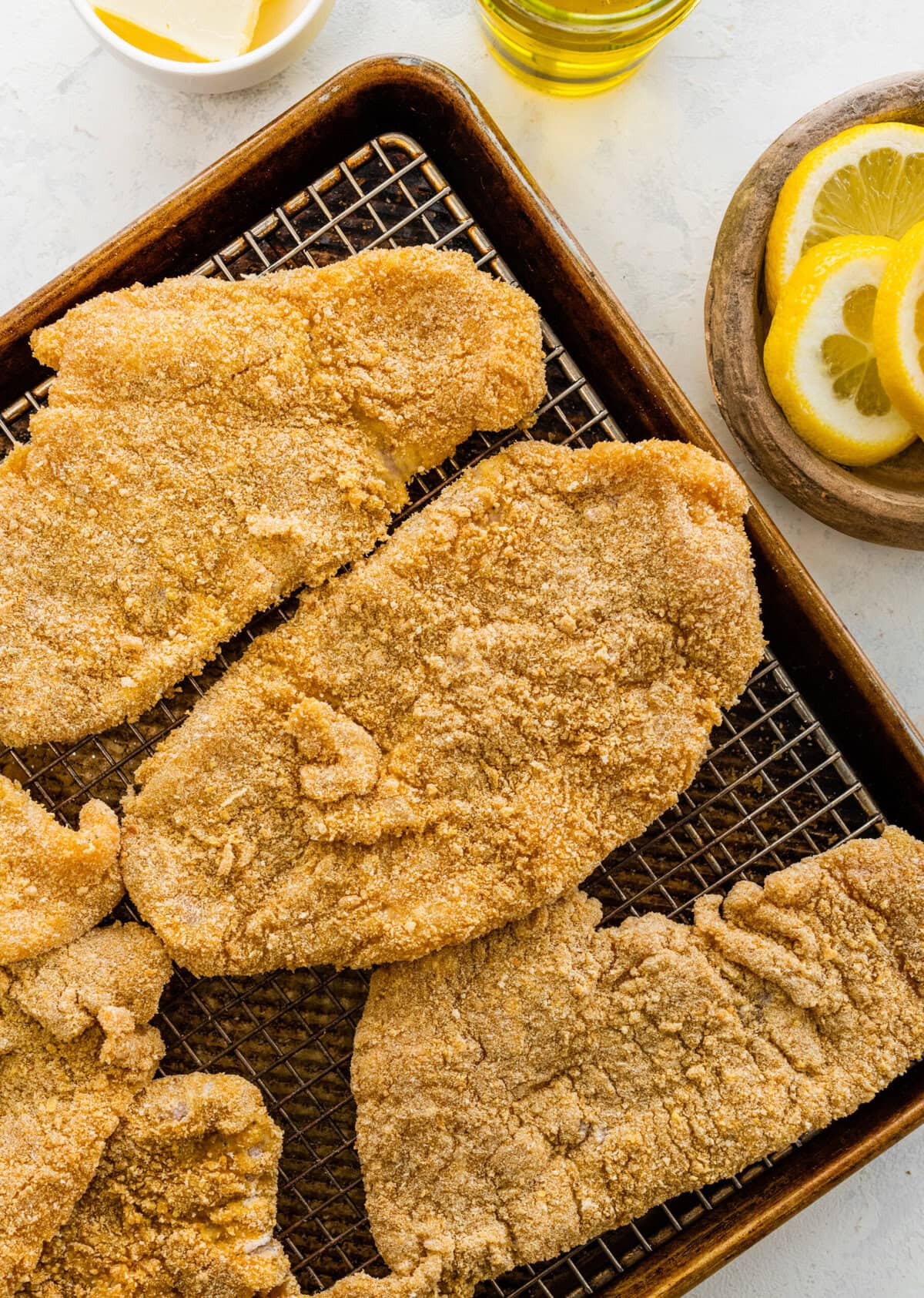 chicken on a wire rack after it has been dipped in the flour, egg, and bread crumbs.
