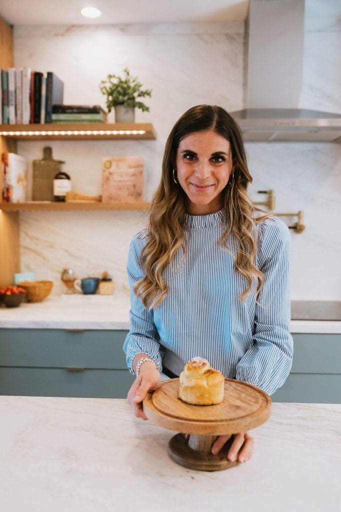woman with brown hair standing in kitchen holding wooden plate with brioche. Perfect Afternoon snack 