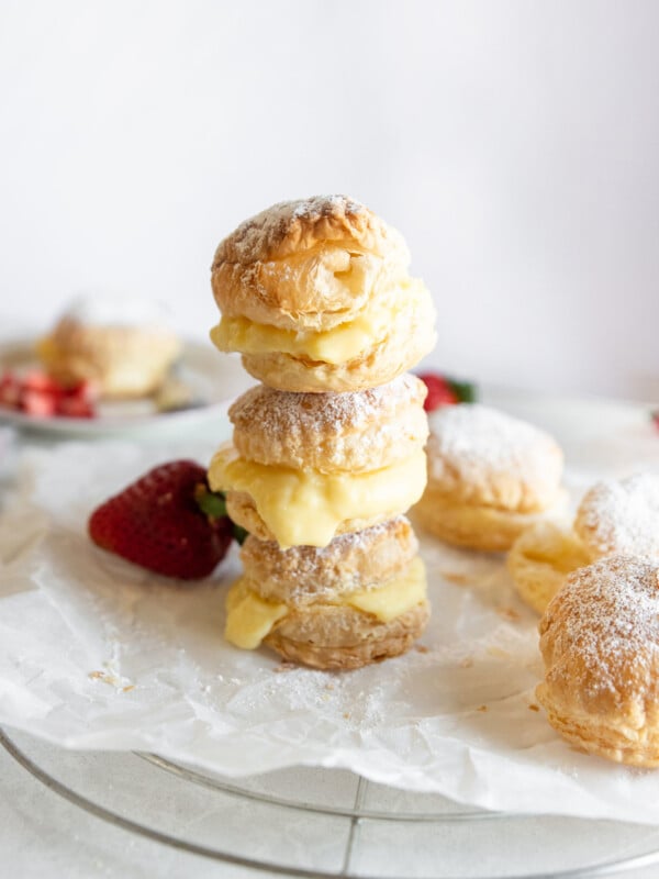 Puff pastry stacked with pastry cream oozing out the sides and strawberries in the background