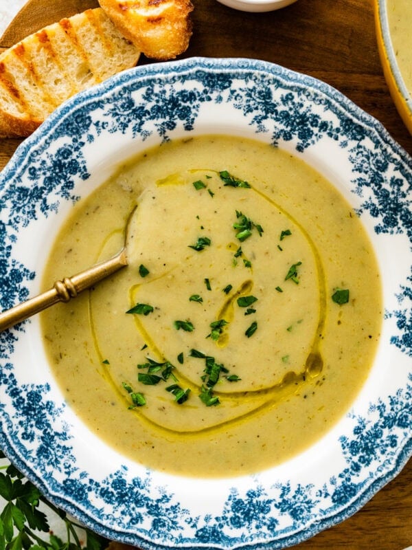 old fashioned white and blue bowl with artichoke soup in it. Spoon bowl. Crusty bread on side.