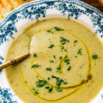 old fashioned white and blue bowl with artichoke soup in it. Spoon bowl. Crusty bread on side.