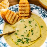 old fashioned white and blue bowl with artichoke soup in it. Spoon bowl. Sliced toasted bread in the bowl.