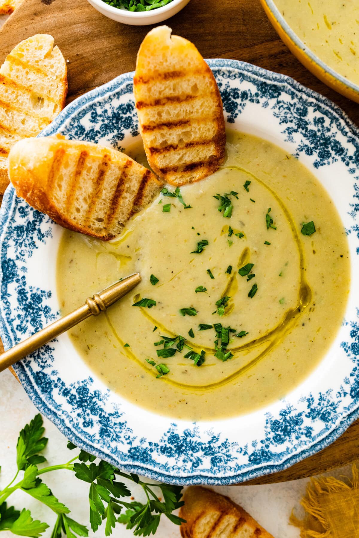 old fashioned white and blue bowl with artichoke soup in it. Spoon bowl. Sliced toasted bread in the bowl.