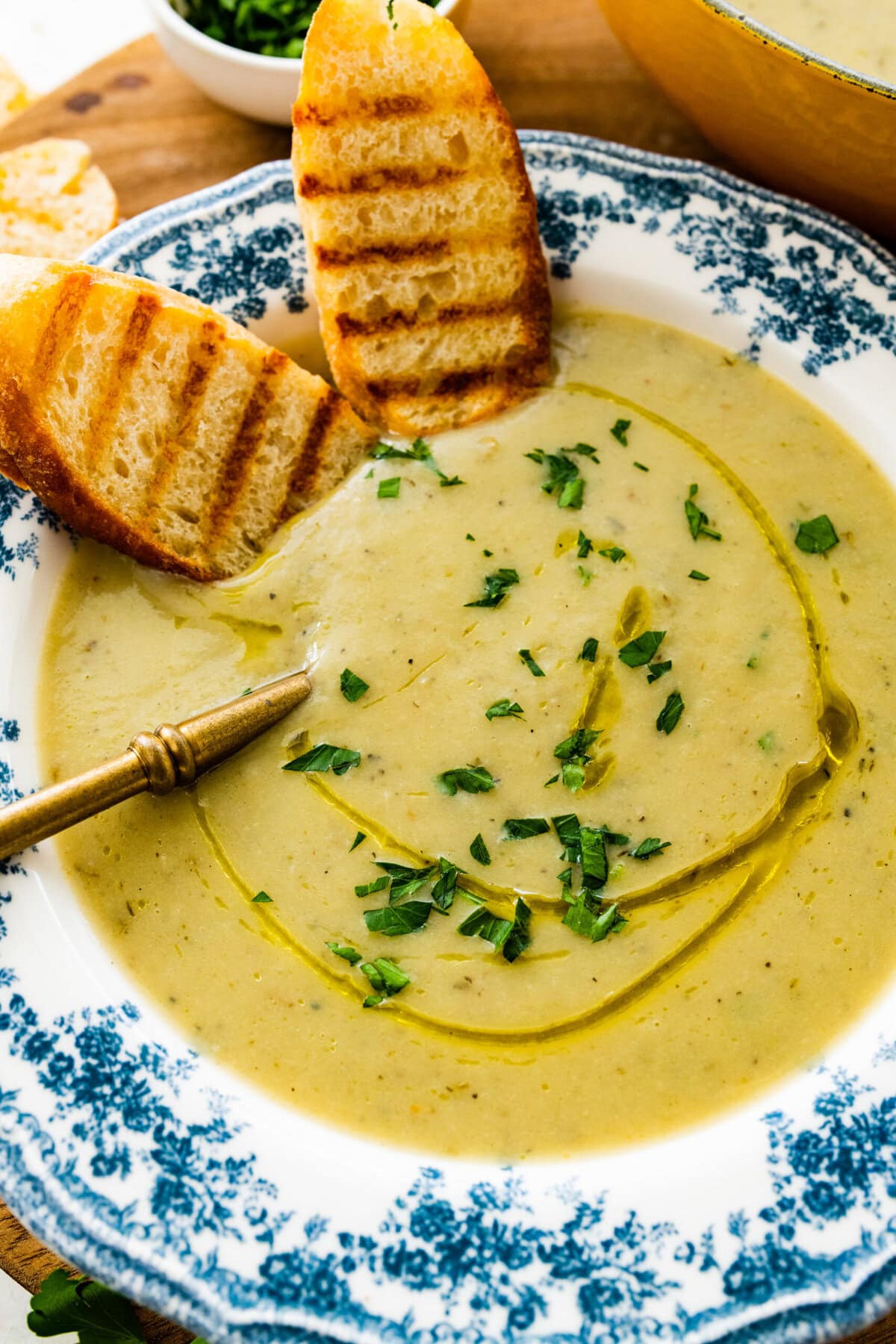 old fashioned white and blue bowl with artichoke soup in it. Spoon bowl. Sliced toasted bread in the bowl.
