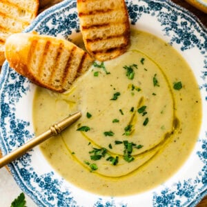 old fashioned white and blue bowl with artichoke soup in it. Spoon bowl. Sliced toasted bread in the bowl.