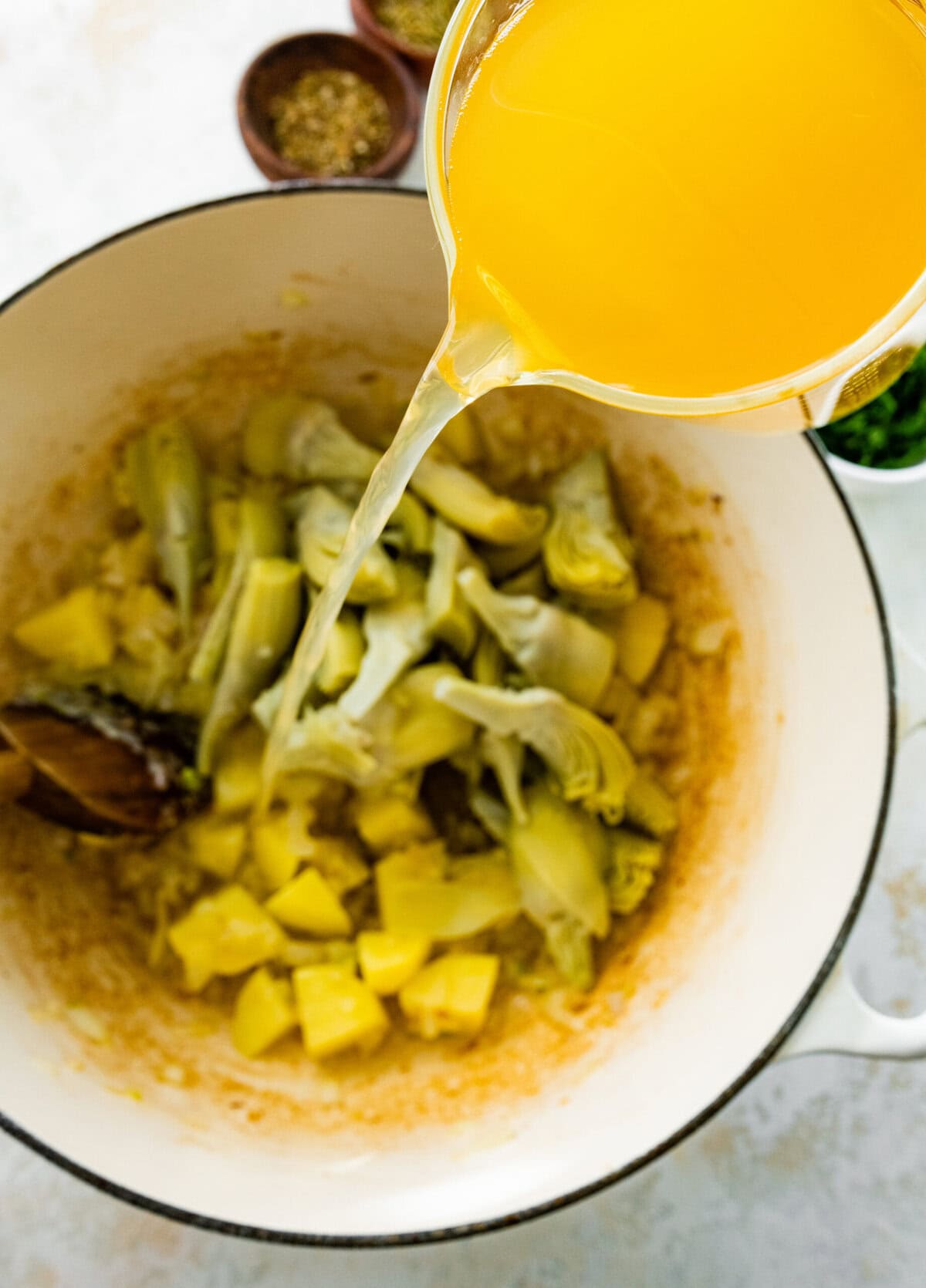 making the artichoke soup- add the broth to the pot.
