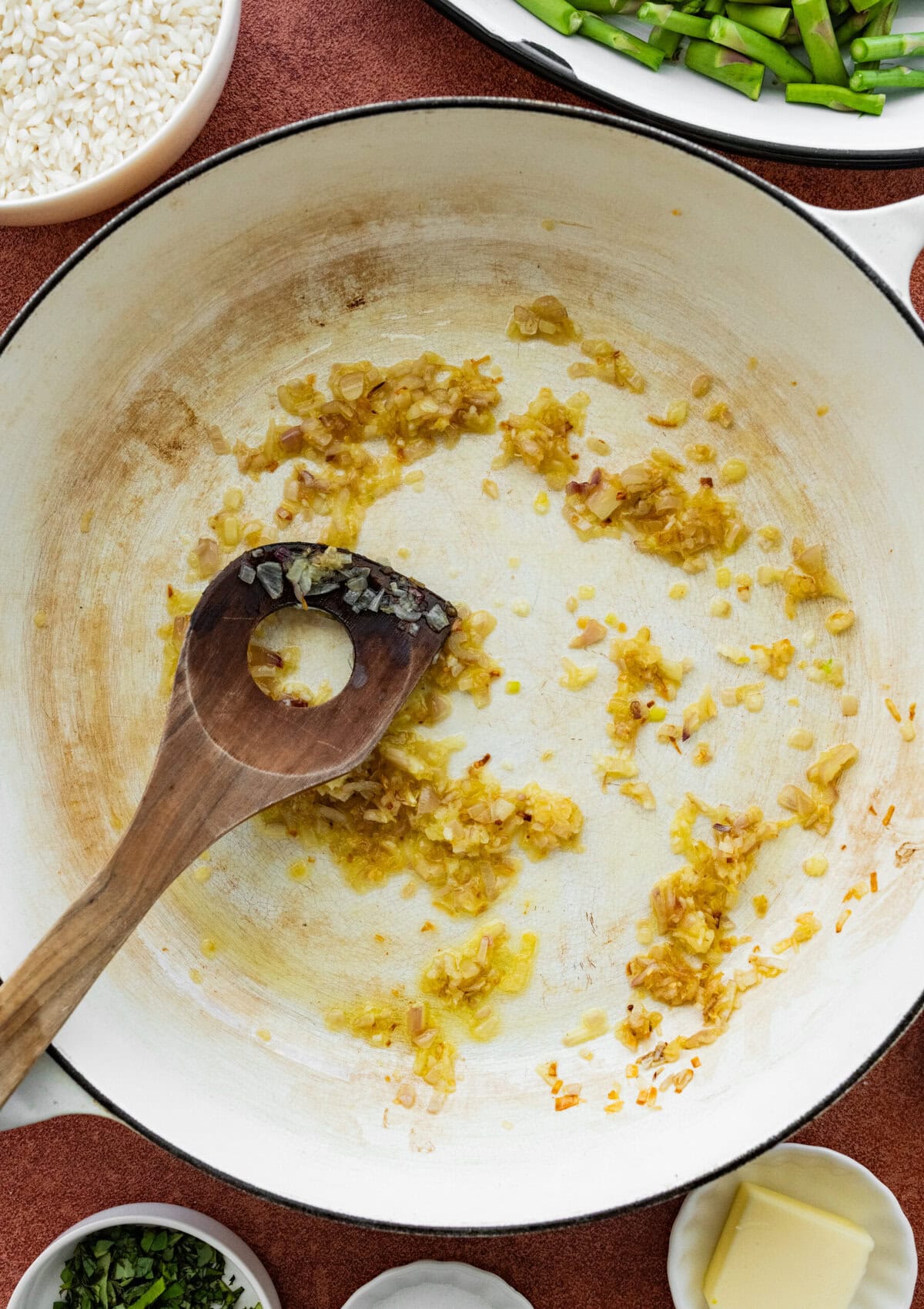 Broth, shallots, and garlic being stirred in a pan.