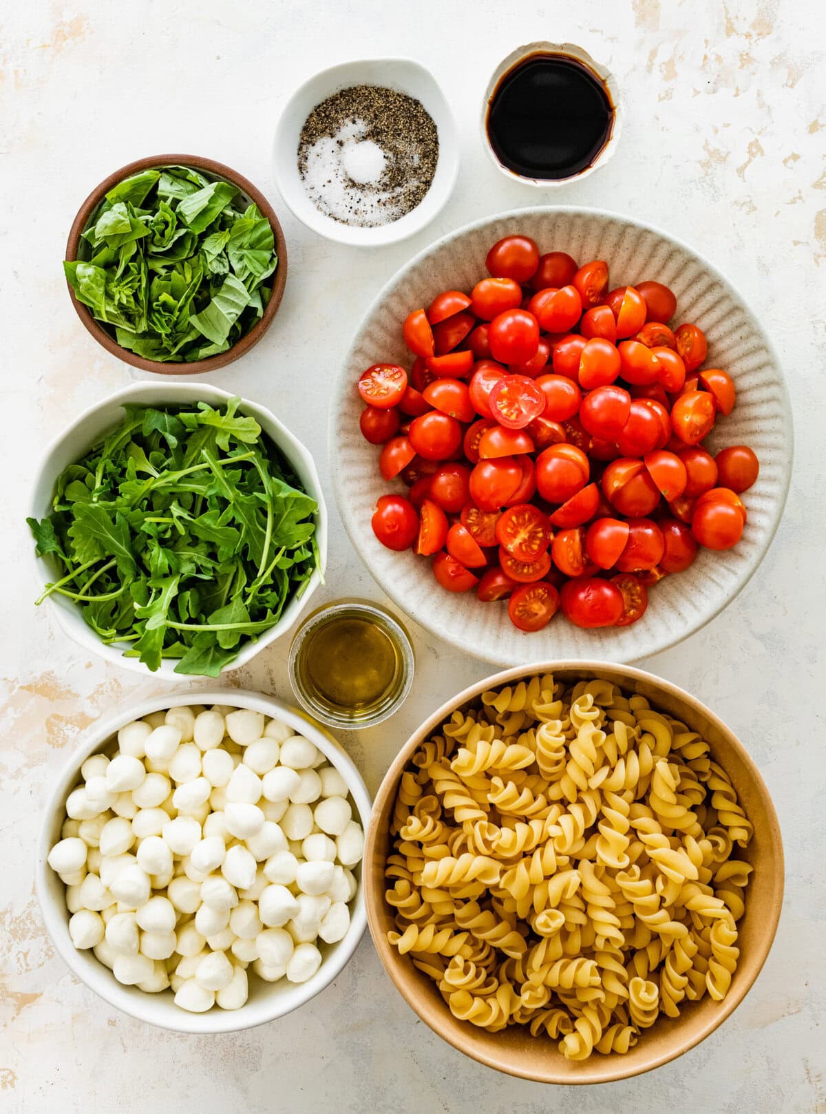 The ingredients for this pasta salad are arranged in bowls.