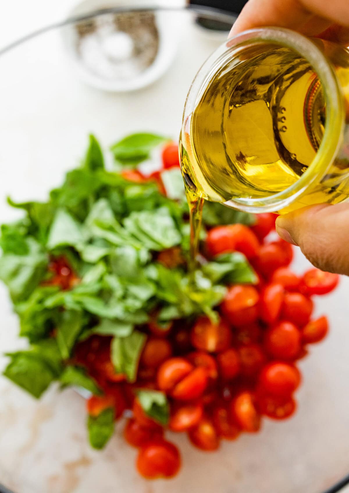 A person pouring olive oil over a bowl of tomatoes.