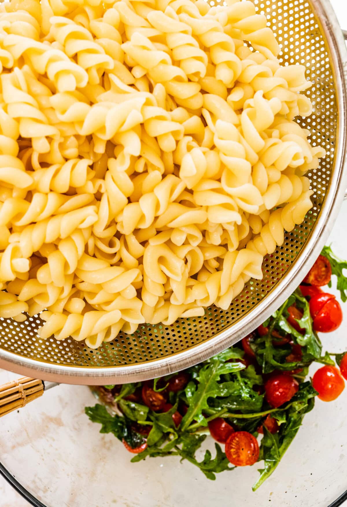 A colander filled with pasta and tomatoes.