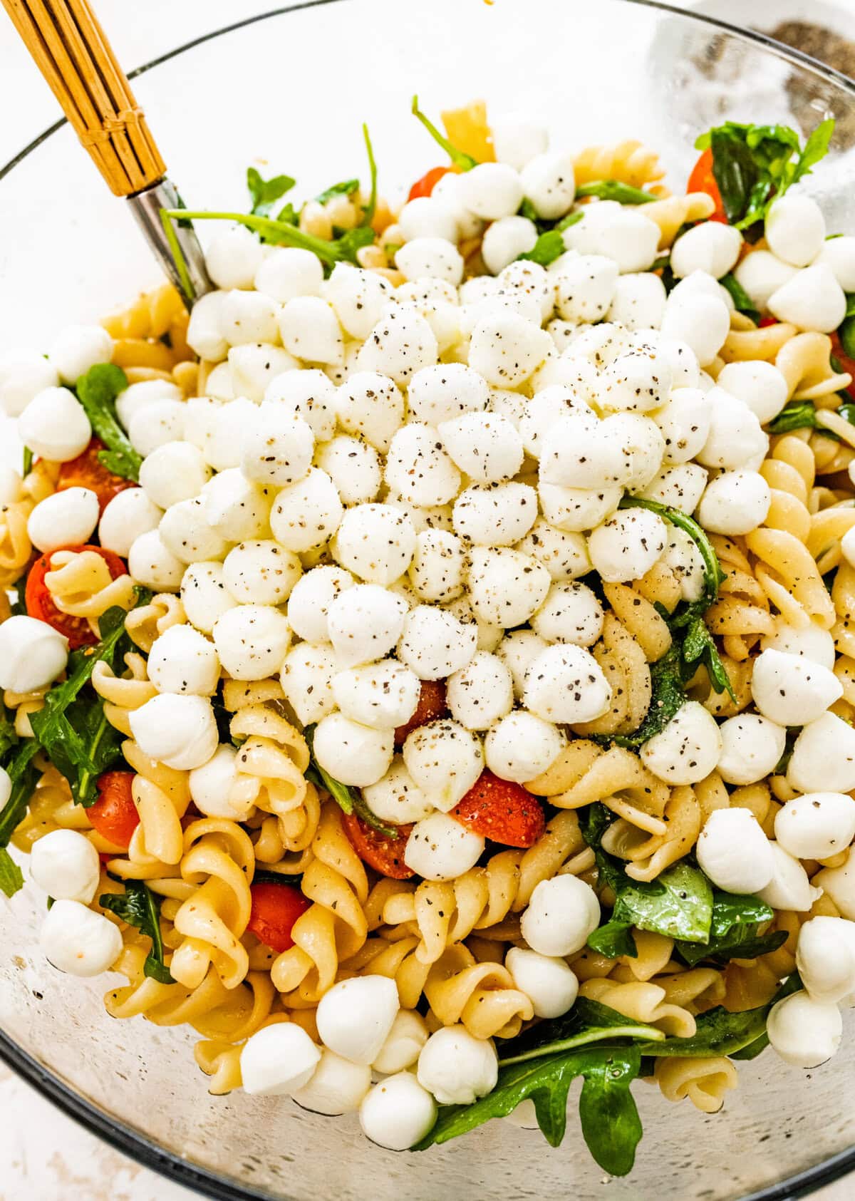 A bowl of pasta salad with mozzarella and tomatoes
