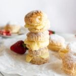 Three cream filled pastries stacked on top of each other on a plate with more ingredients nearby.
