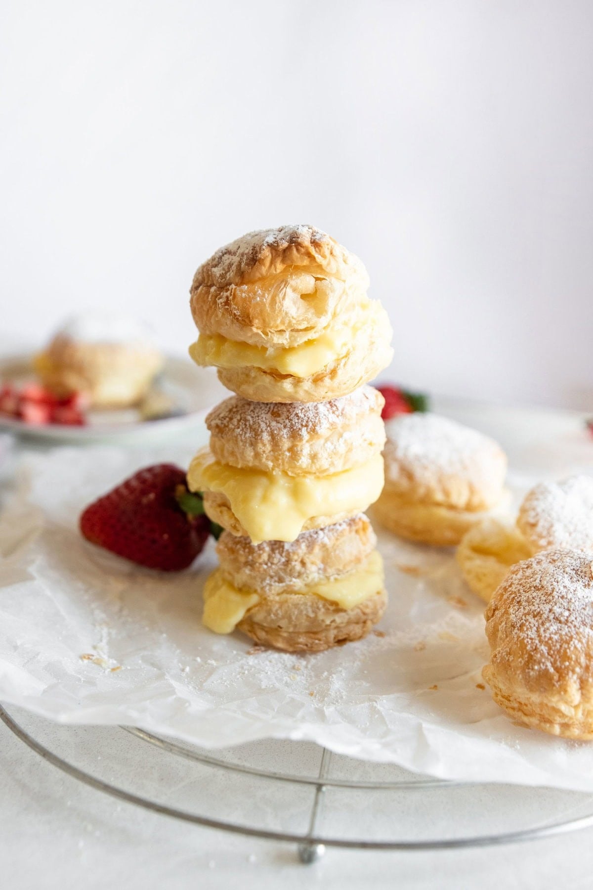 Three cream filled pastries stacked on top of each other on a plate with more ingredients nearby.