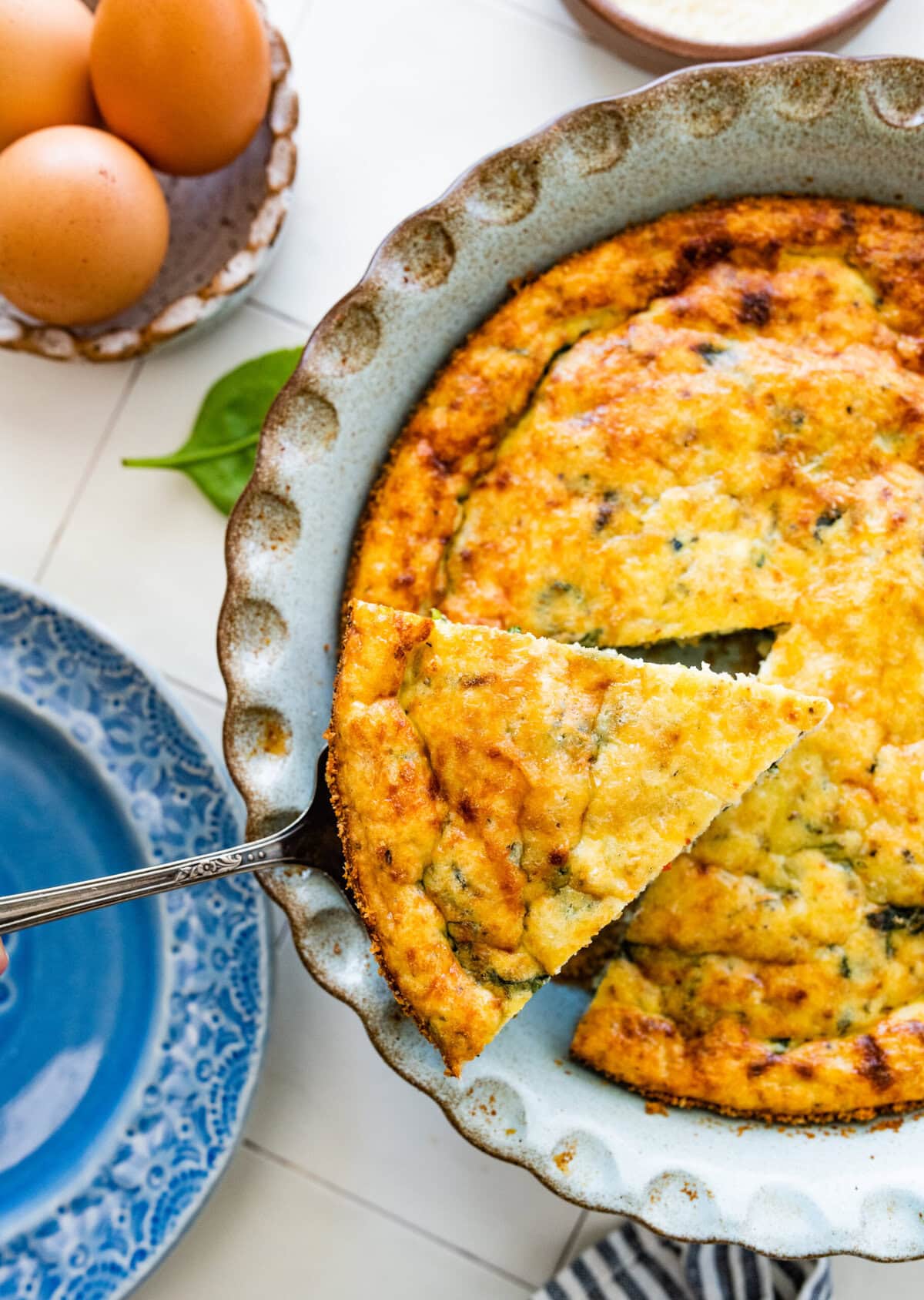 A spatula lifting a serving of Italian spinach frittata from the dish.