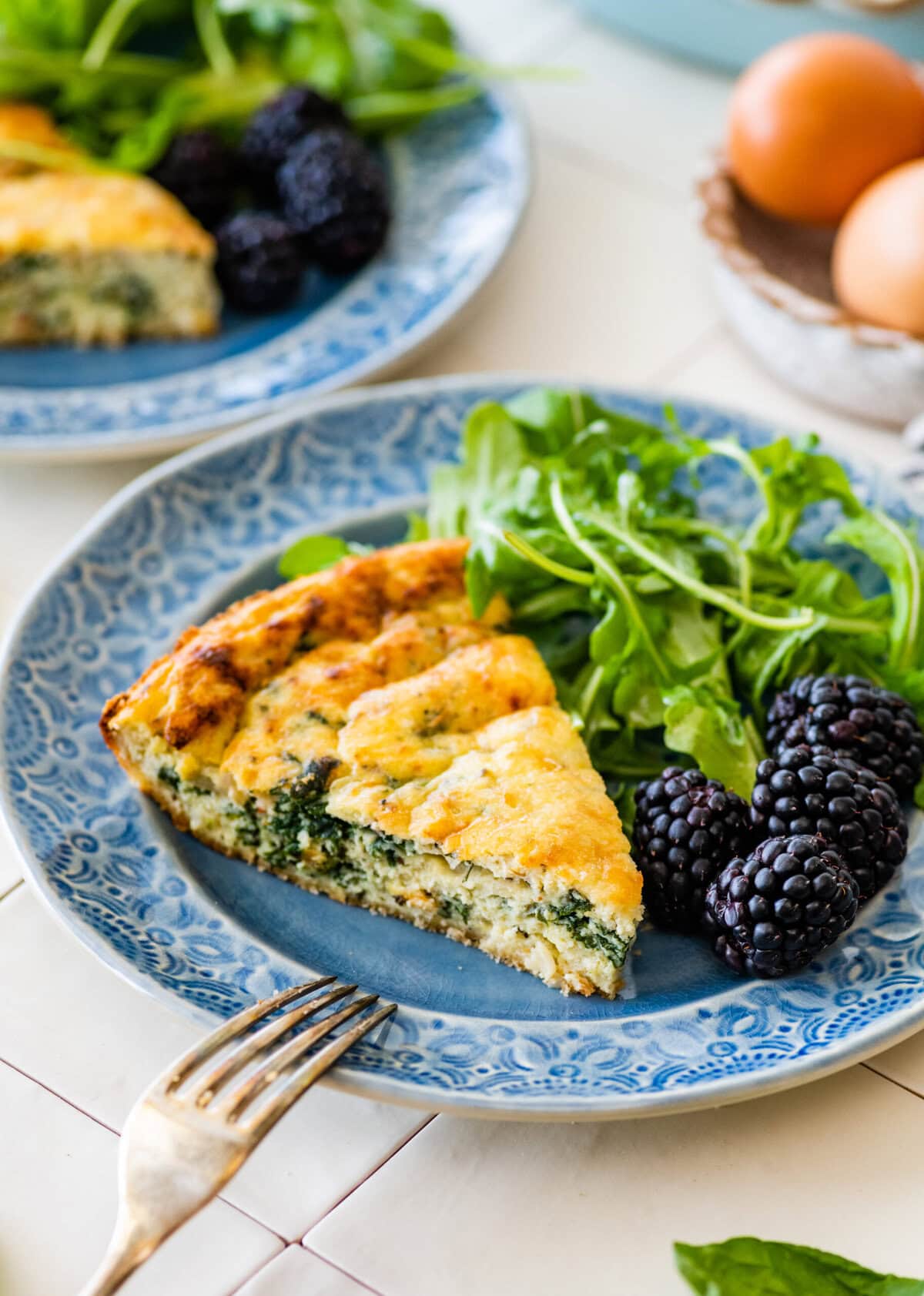 A slice of Italian spinach frittata on a blue plate with a fork resting on the edge.