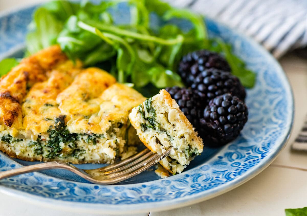 An Italian frittata with spinach and ricotta on a plate with greens and fruit.