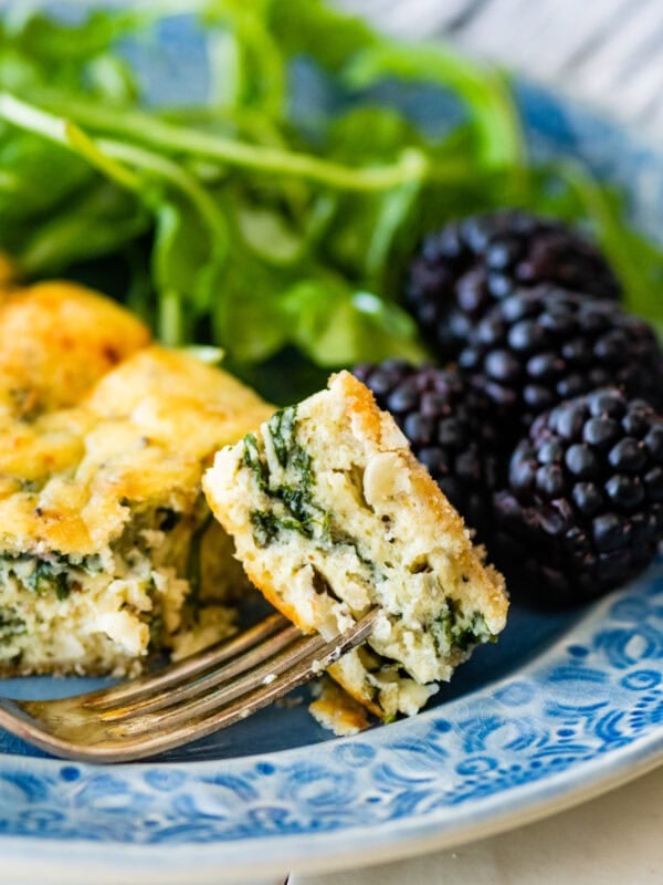 A piece of spinach frittata on a plate with a bite on a fork.