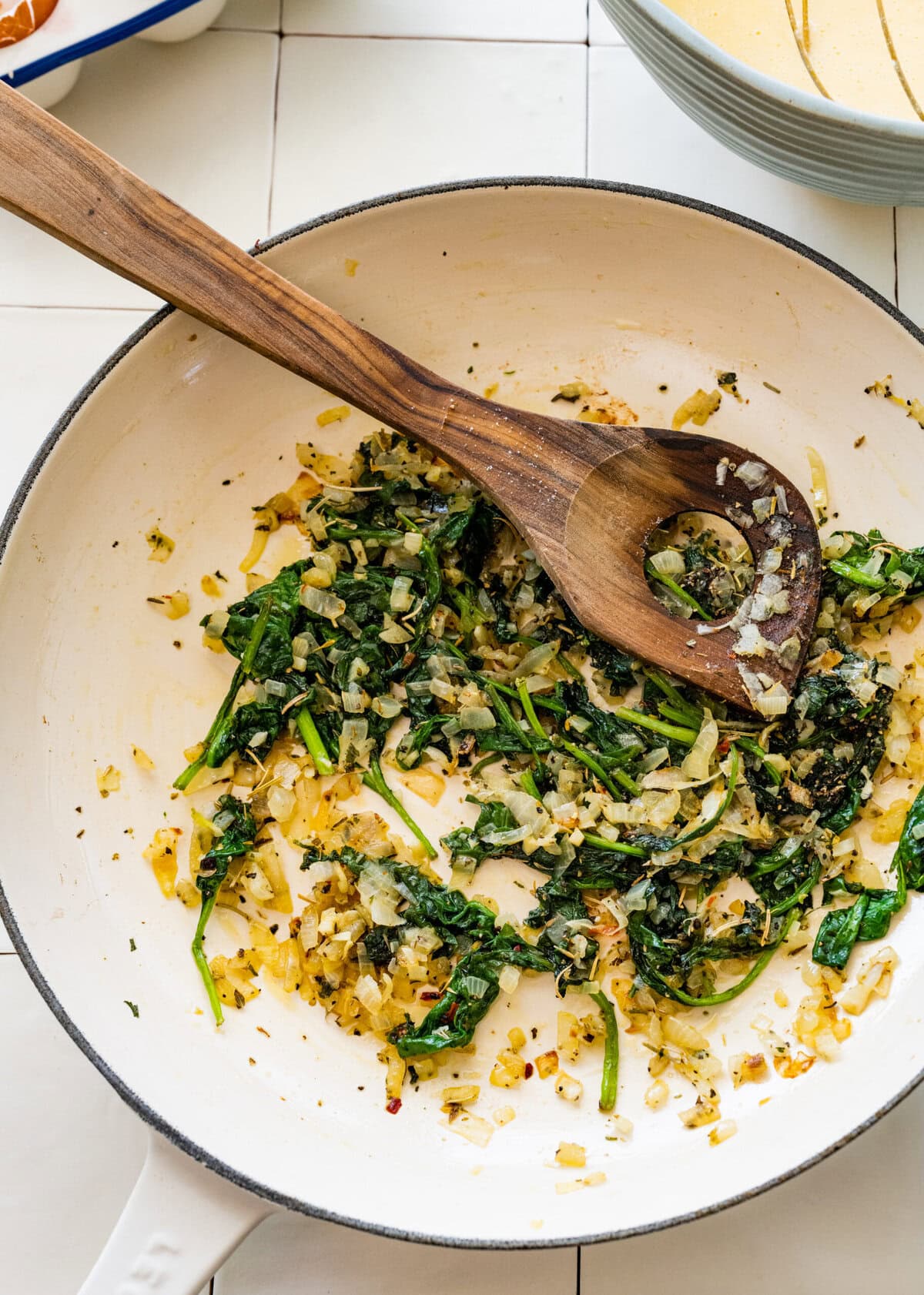 Cooked spinach and onions in a skillet with a wooden spoon.