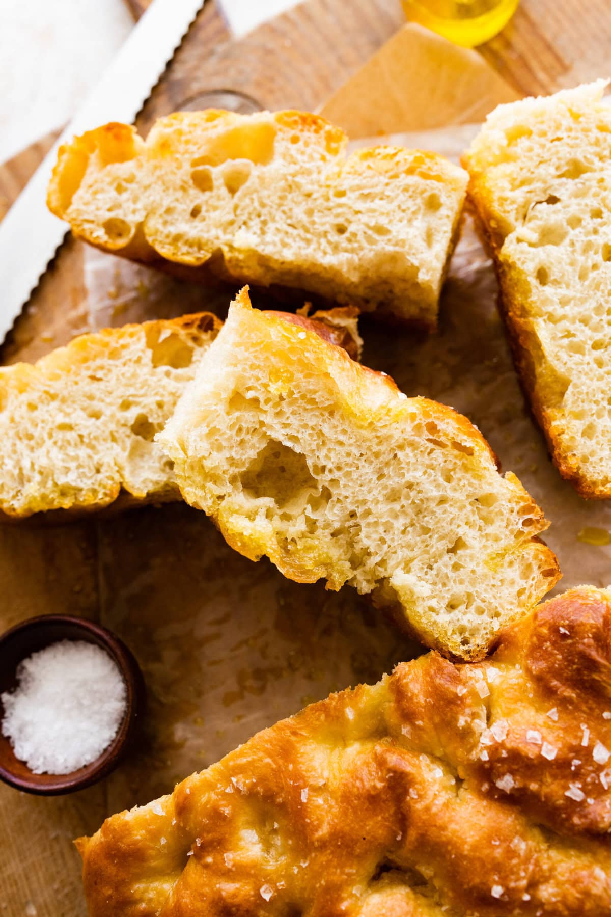 focaccia bread in slices on a wooden board with salt on the side.