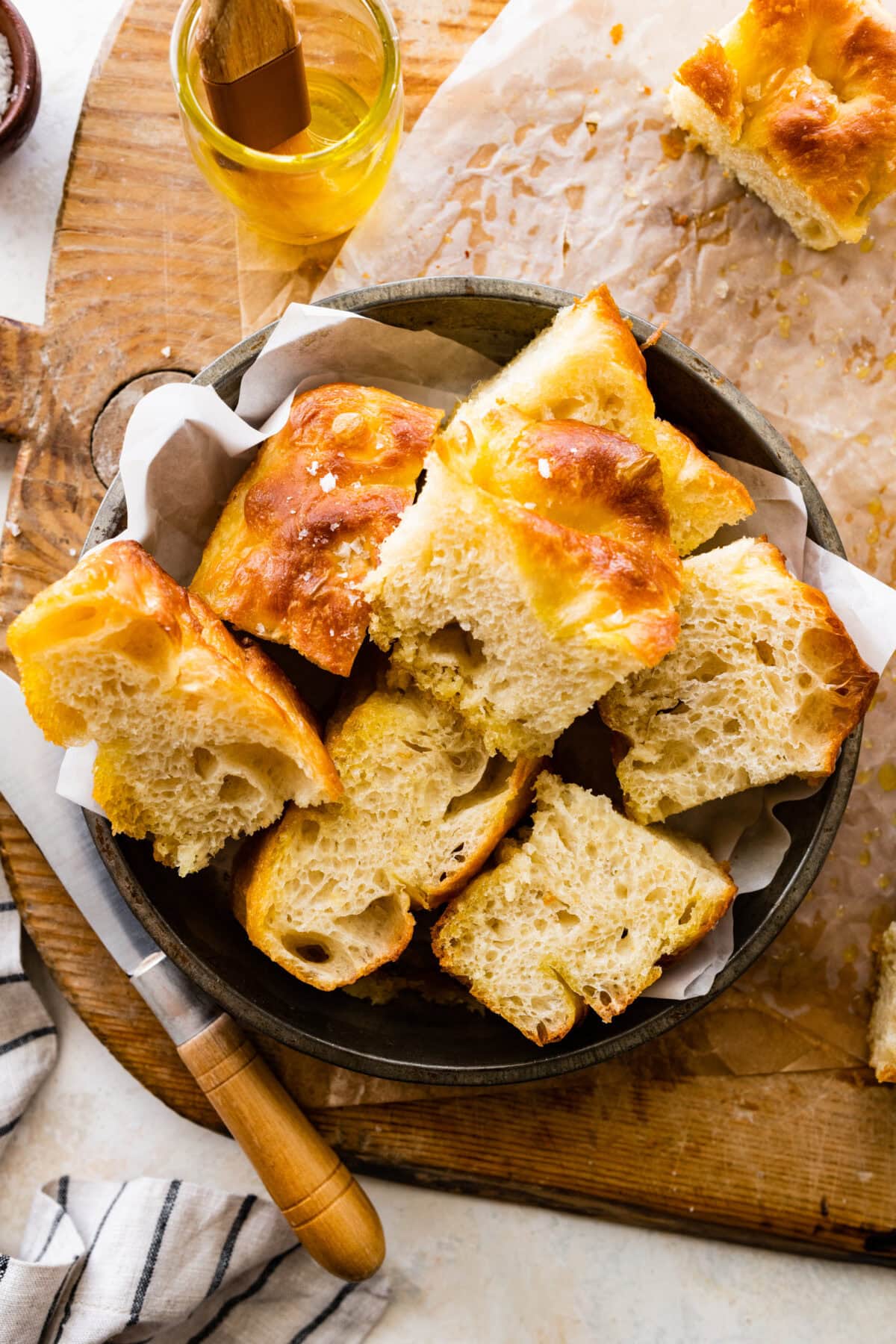 Slices of no knead focaccia in a bread basket on top of a wooden board. The focaccia slices are nice and airy!