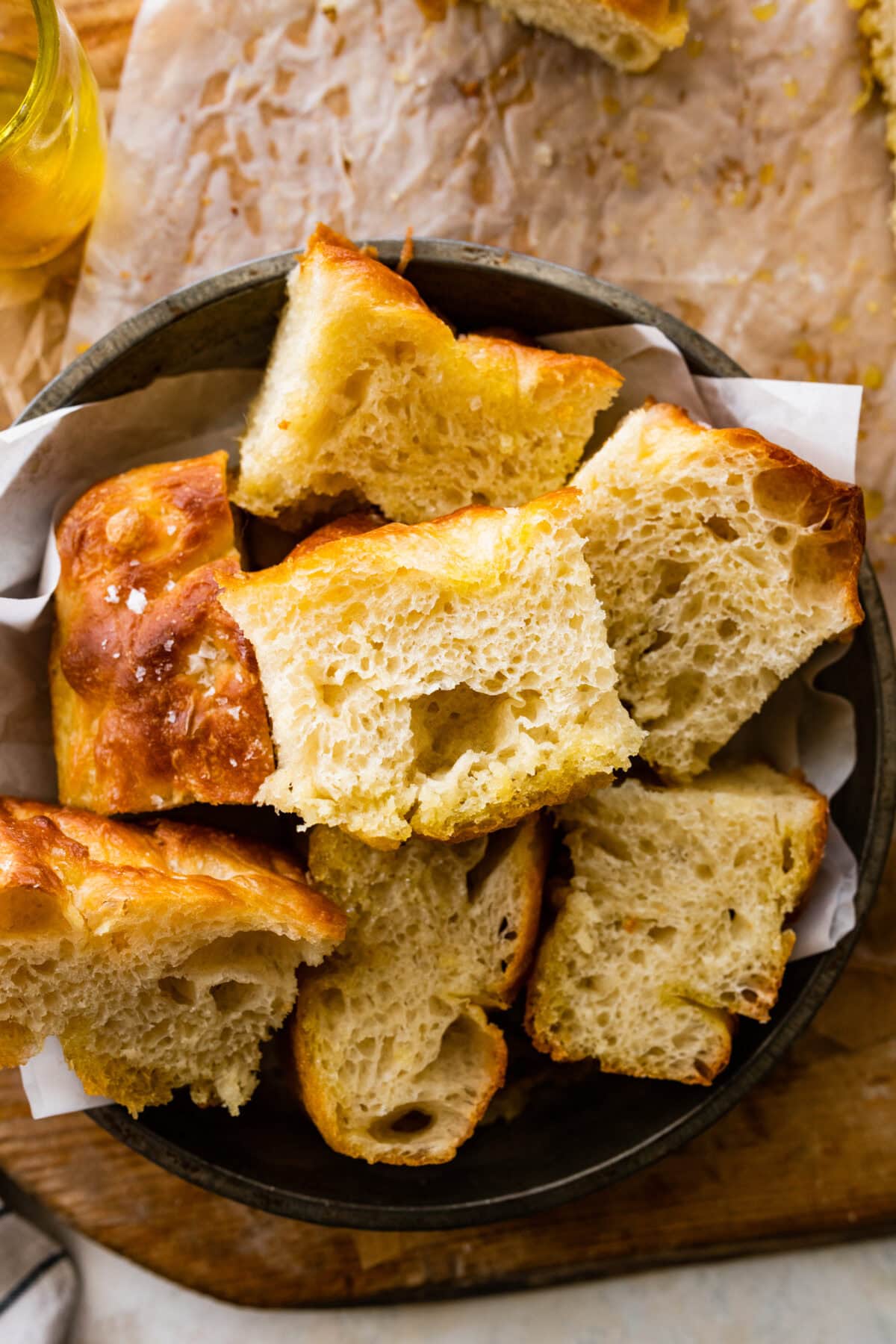 Slices of no knead focaccia in a bread basket on top of a wooden board. The focaccia slices are nice and airy!