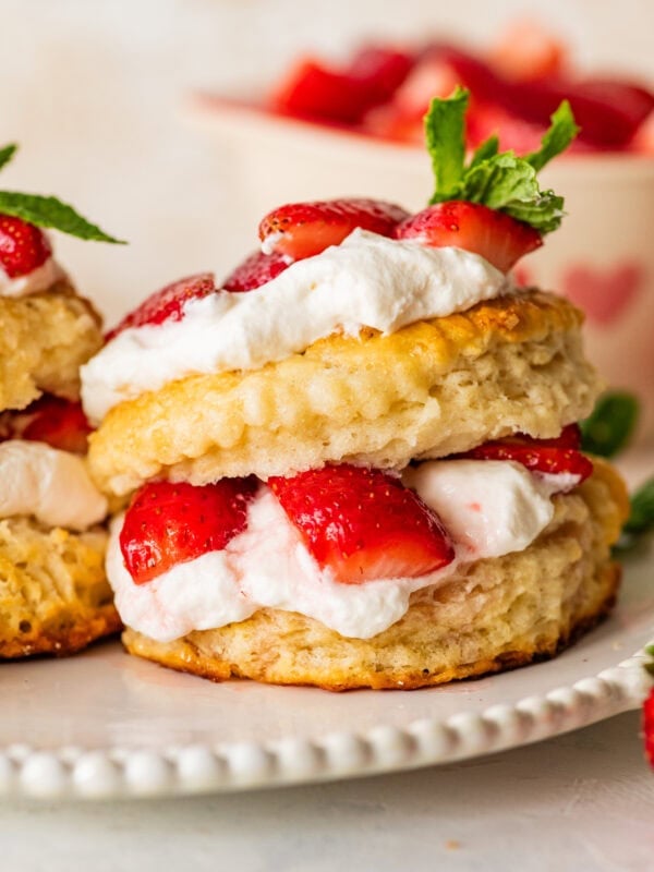 A strawberry shortcake biscuit on a plate with more ingredients for the recipe nearby.