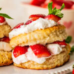 A strawberry shortcake biscuit on a plate with more ingredients for the recipe nearby.