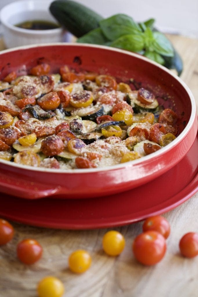 Baked zucchini and tomato bruschetta in a round red pan.