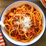 A platted bowl of Bucatini all’Amatriciana in a white and blue bowl with a fork in it.
