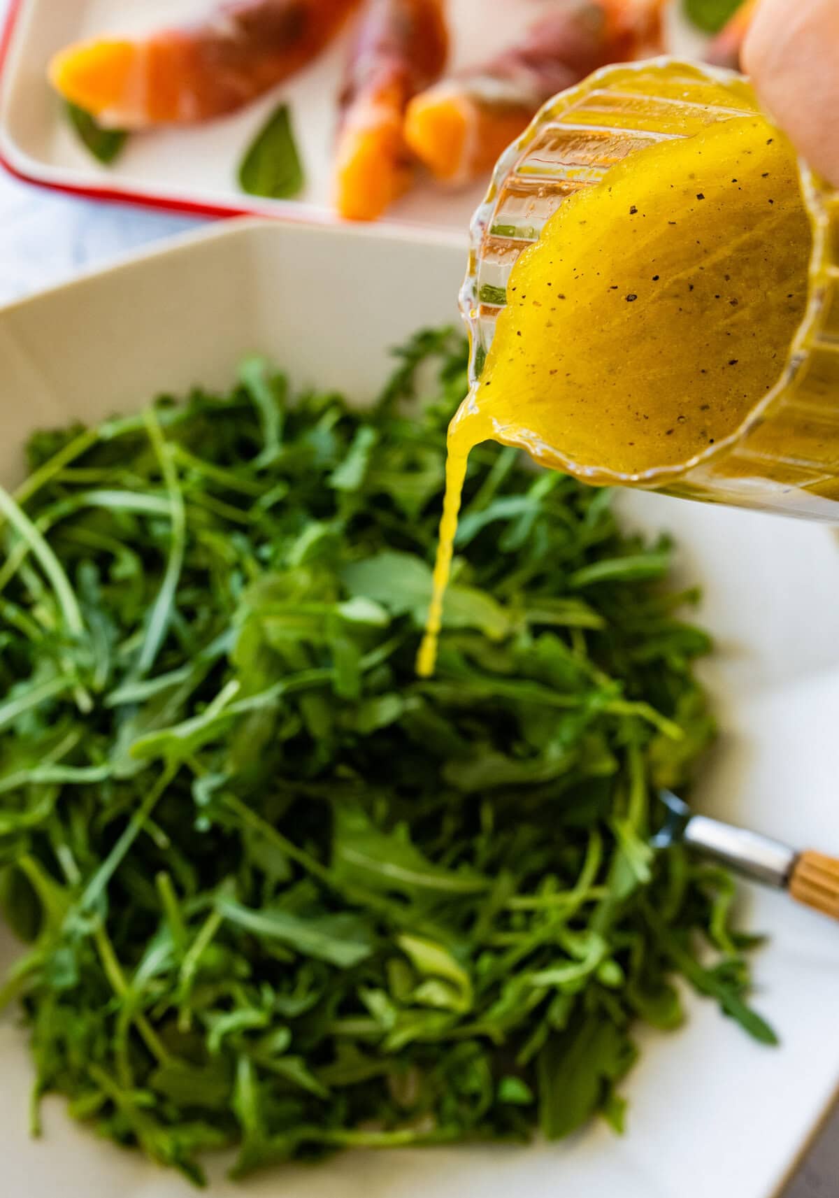 A person pouring mustard over a salad.