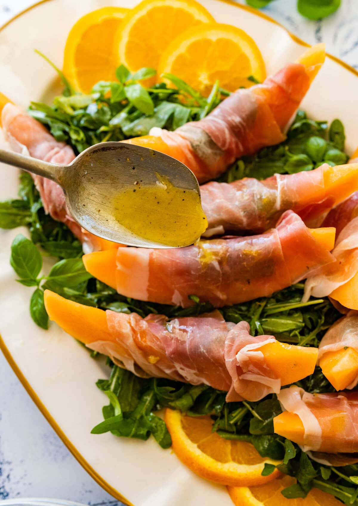 A plate of sliced ham and greens with orange slices.