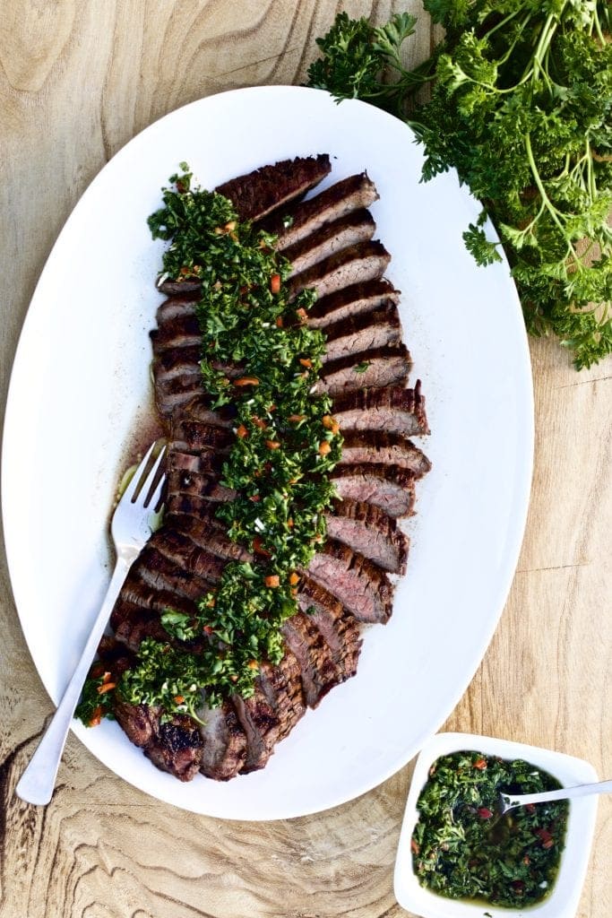 Tri-tip steak and chimichurri sauce cut on a plate with curly parsley on the side. 
