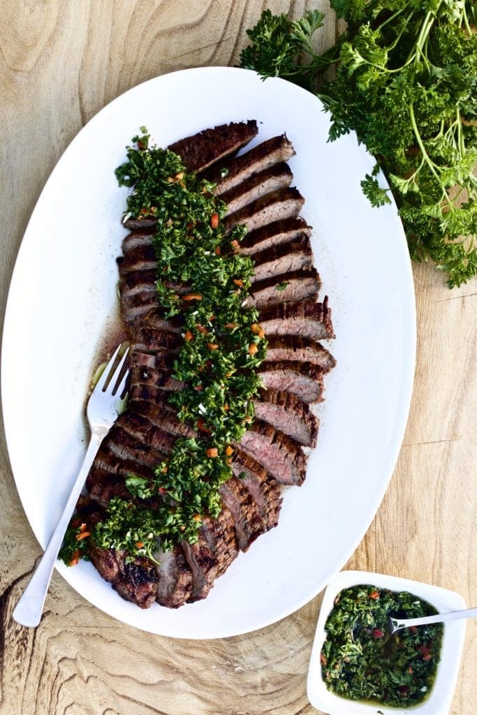 Tri-tip steak and chimichurri sauce cut on a plate with curly parsley on the side.