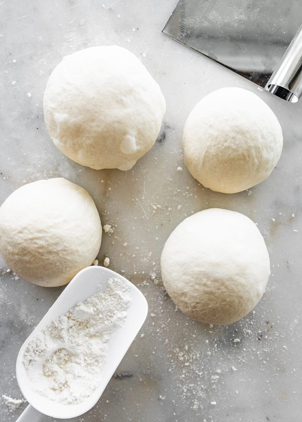 Four dough balls on a counter with a measuring cup