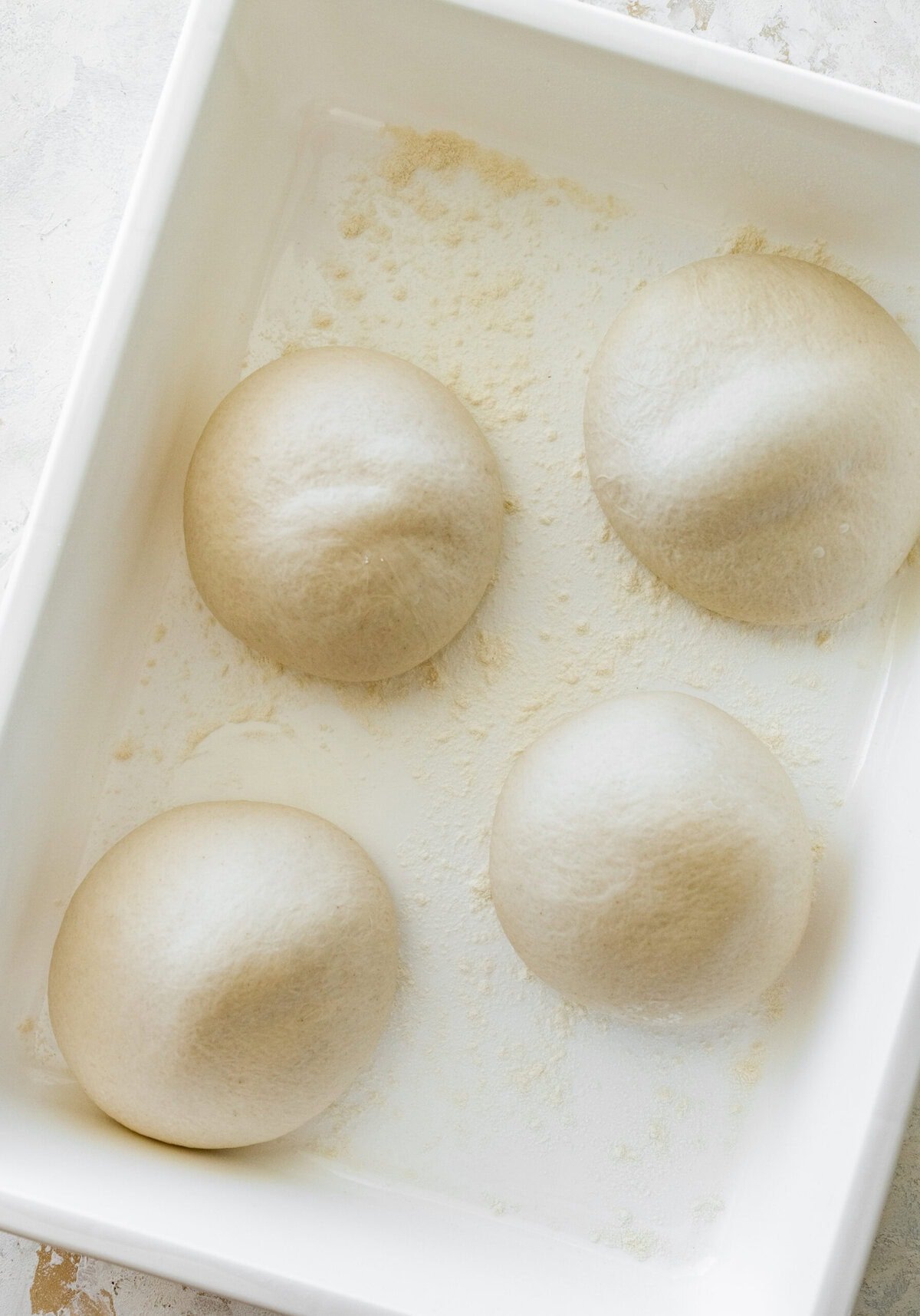 Four balls of dough in a white container that are risen.