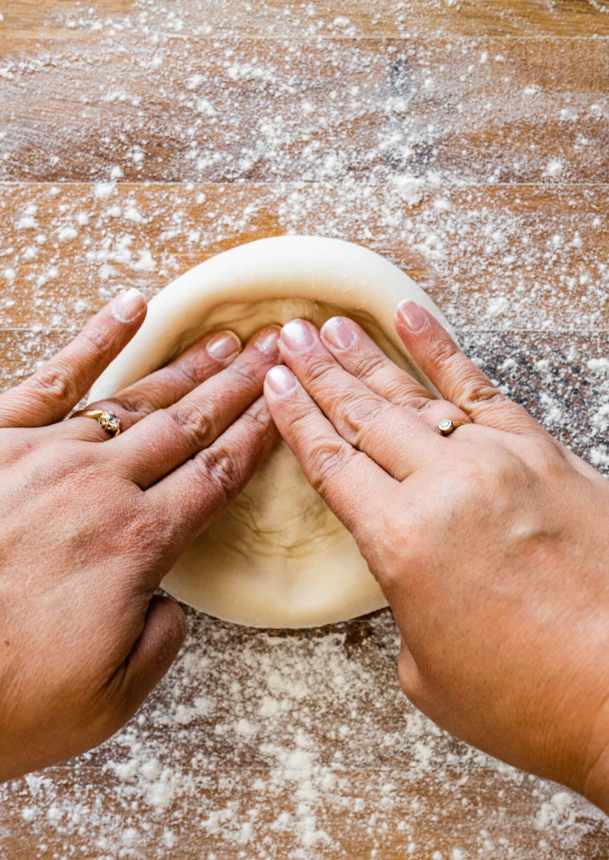 Hands of a woman kneading dough on a wooden table.