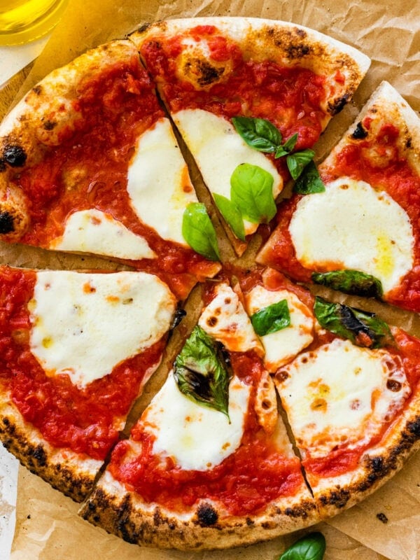 A margherita pizza with cheese and basil leaves on a table cut into slices. Neapolitan pizza.