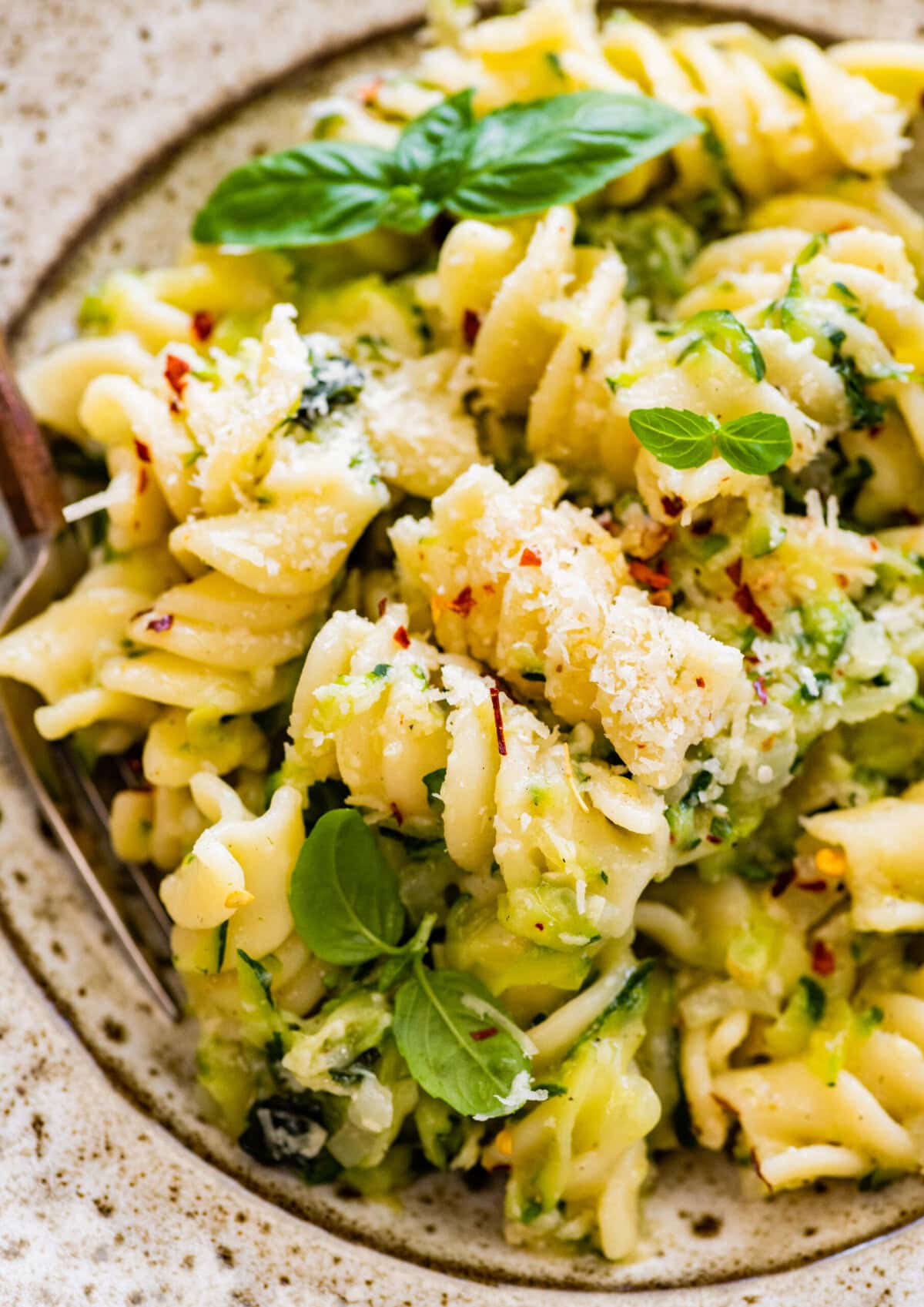 Pasta with zucchini and cheese in a bowl with a fork in it. Red pepper flakes as garnish.