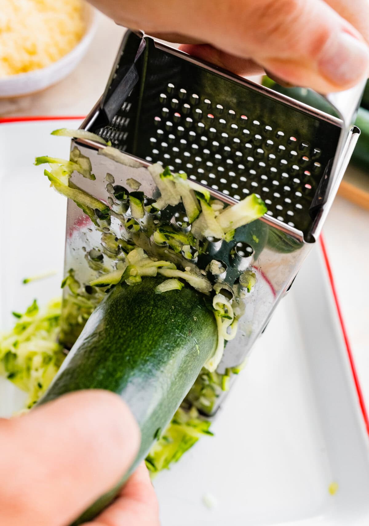 A person is using a grater to cut up a zucchini.