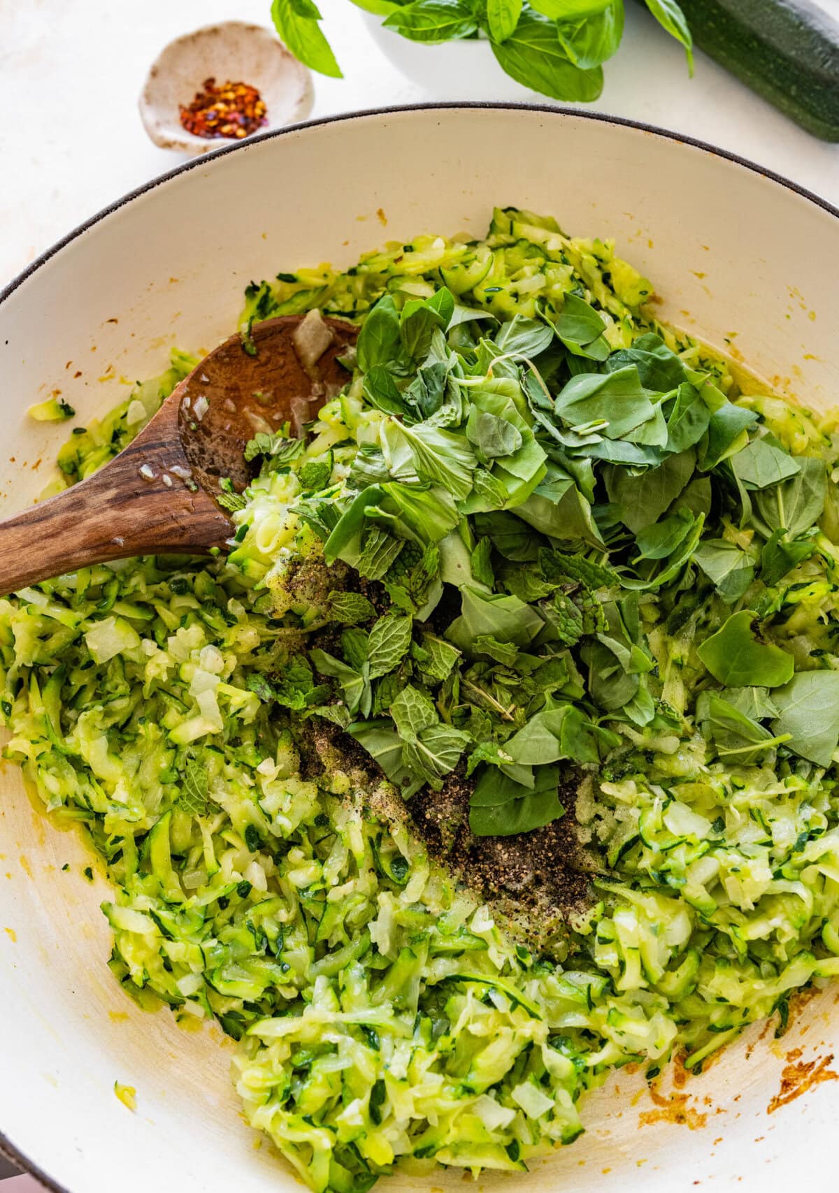 Pan with wooden spoon stirring the zucchini and basil.