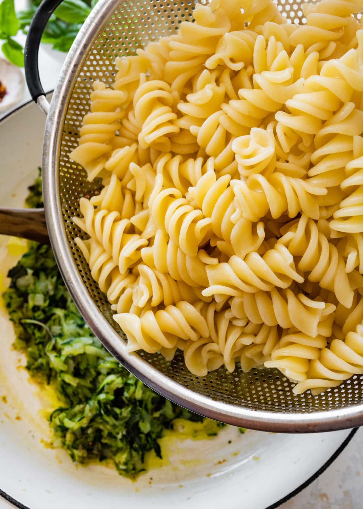 Adding hot pasta to the cooked zucchini mixture in the pan.