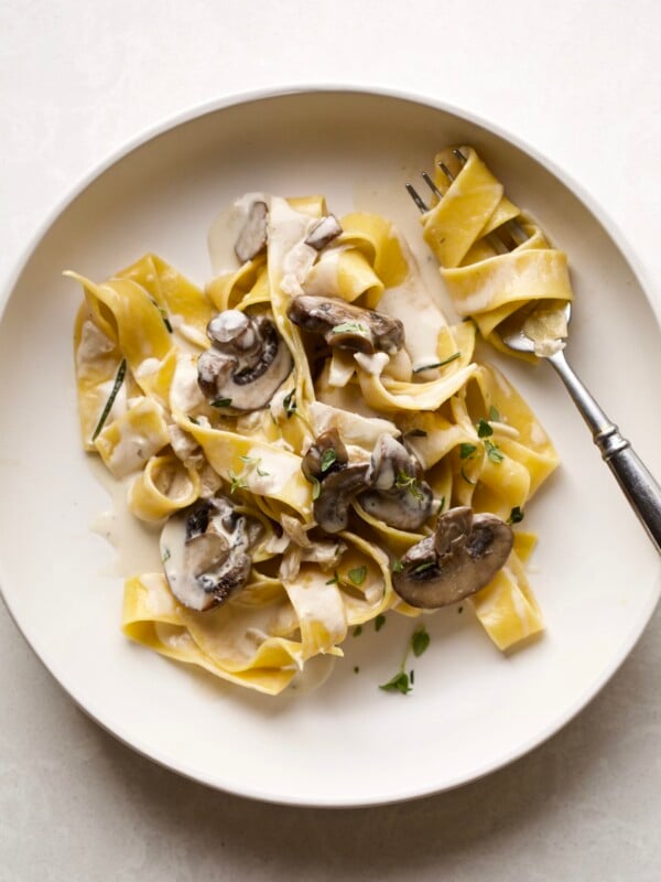 Fork swirled with creamy pappardelle pasta with mushrooms on a plate.