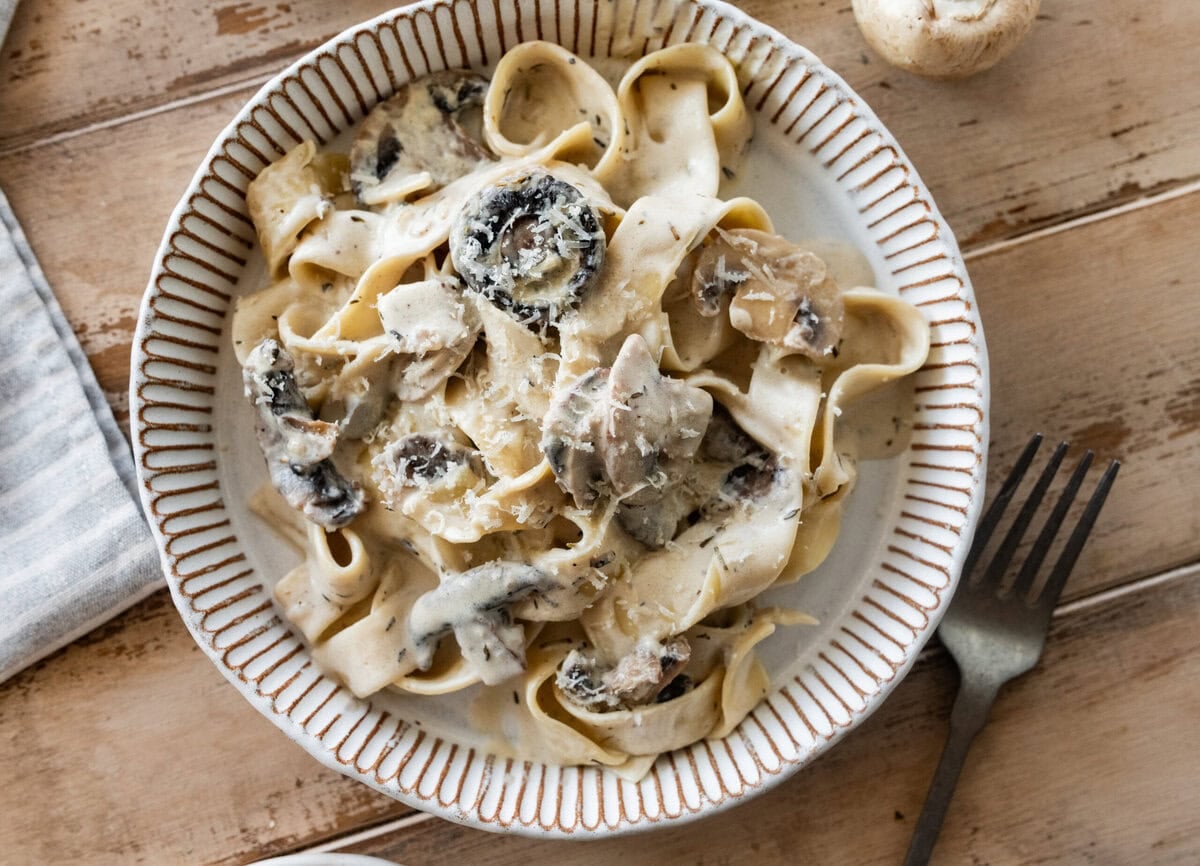creamy pappardelle pasta with mushrooms in a bowl with silverwear nearby. 