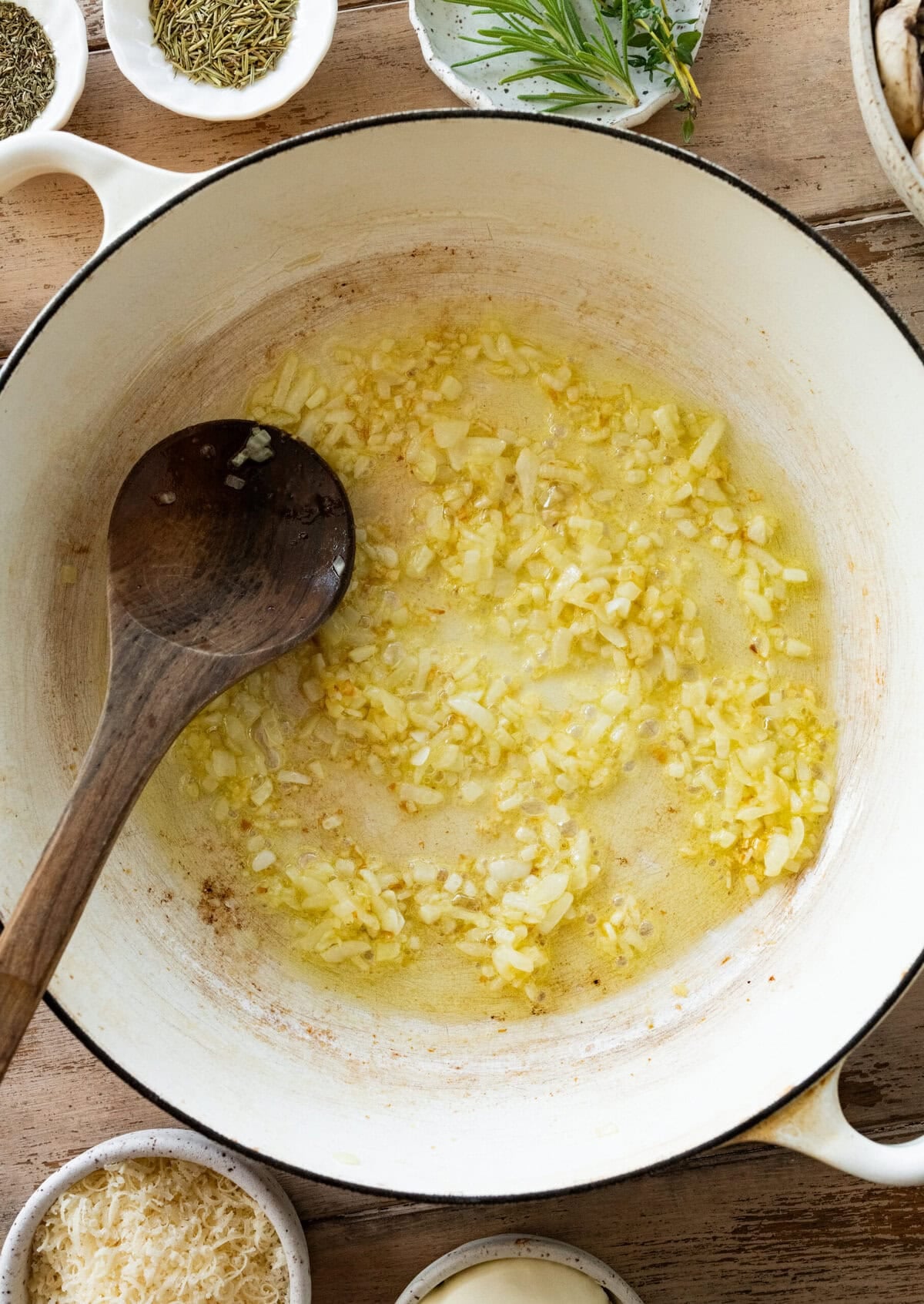 garlic, onions and olive oil in a large pot with more ingredients nearby and a spoon resting inside.