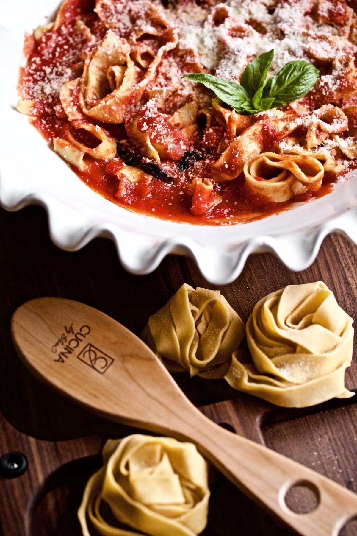 Homemade pappardelle pasta on a table and in a bowl with sauce.