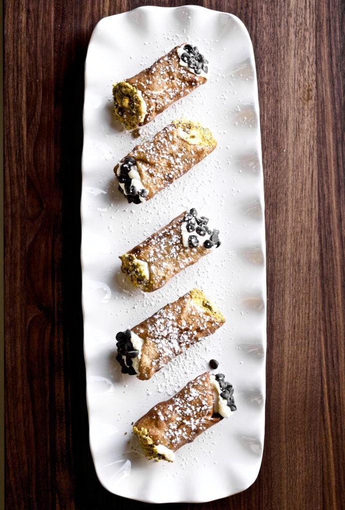 6 cannoli on a plate with pistachios and chocolate chips on the ends