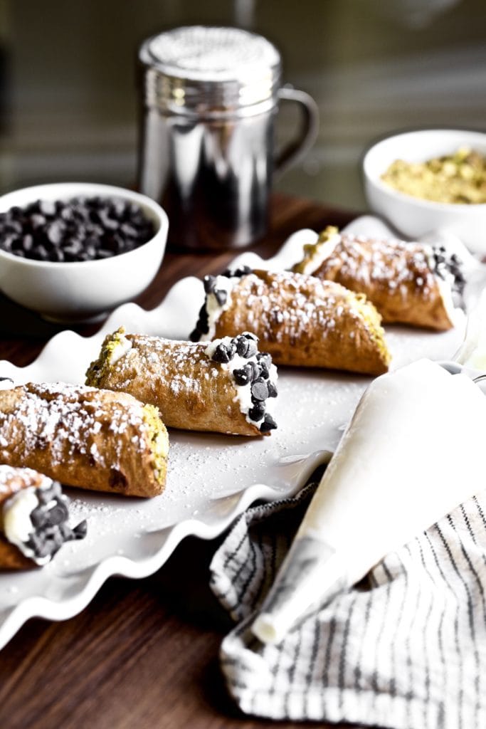 Cannoli on a white plate with a piping bag.