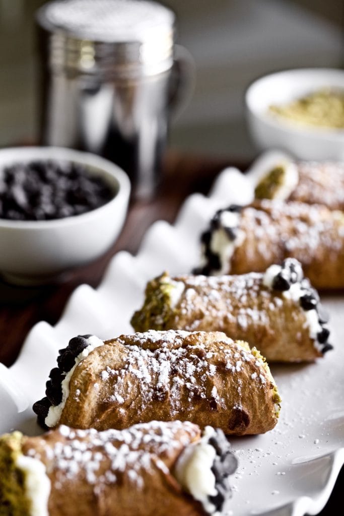 Cannoli on a plate with pistachios and chocolate chips on the ends on a white plate.