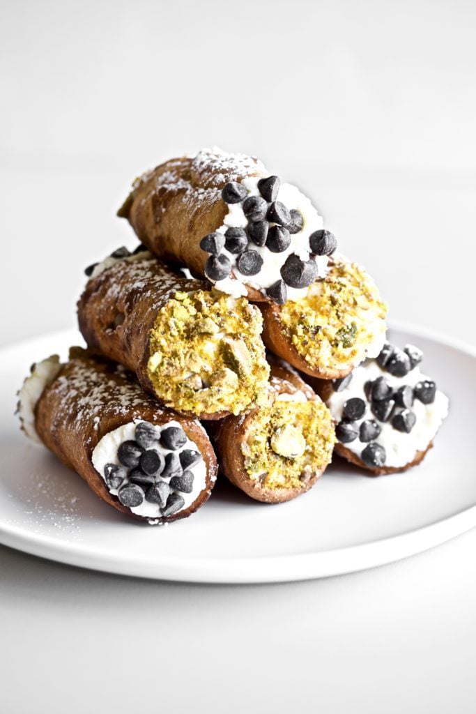 6 cannoli on a plate with pistachios and chocolate chips on the ends