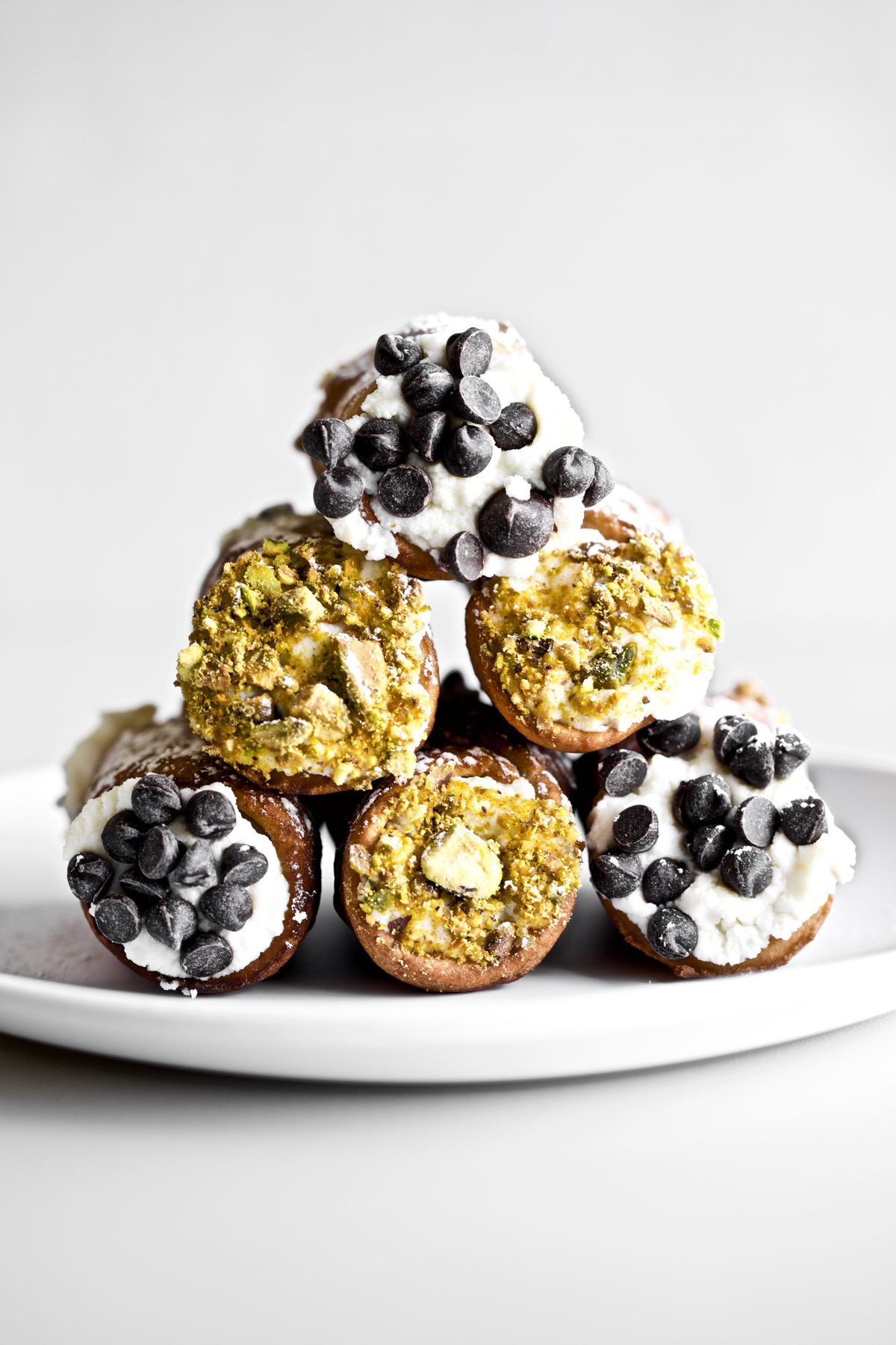 Sicilian cannoli stacked in a pyramid on a white plate.